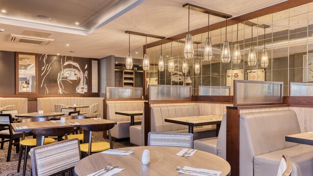 A restaurant with round tables, cushioned booths, and hanging pendant lights. - Premier Inn Cambridge - A14 J32 (Cambridge)