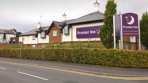 Egy feltűnő táblával, téglafalas homlokzattal és az út mentén húzódó sövényekkel ellátott Premier Inn szálloda.