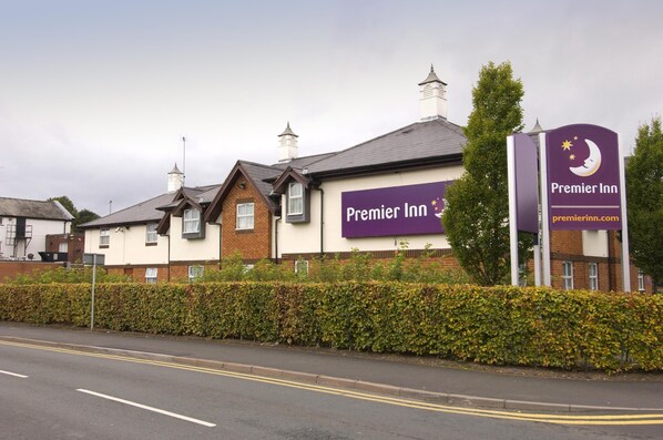 Un hotel Premier Inn con un cartel llamativo, fachada de ladrillo y un seto a lo largo de la carretera.