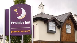Egy Premier Inn tábla, rajta sarlóhold és csillagok, egy téglából épült épület fehér ablakokkal, és egy sövény az előtérben.