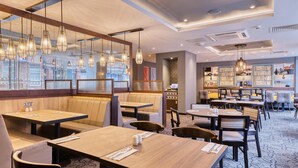 A restaurant with booths, tables, hanging lights, and a view of the outside. - Premier Inn Chester - Railway Station (Chester)
