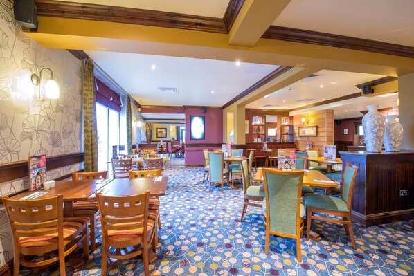 A hotel lobby with wooden tables and chairs, patterned floor tiles, and a reception area with a counter and decorative vases. - Premier Inn Cleethorpes (Cleethorpes)
