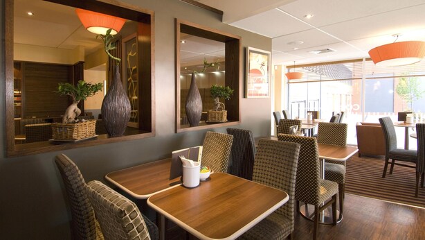 L’intérieur d’un restaurant avec des tables et des chaises en bois, de grands miroirs et des lampes suspendues.