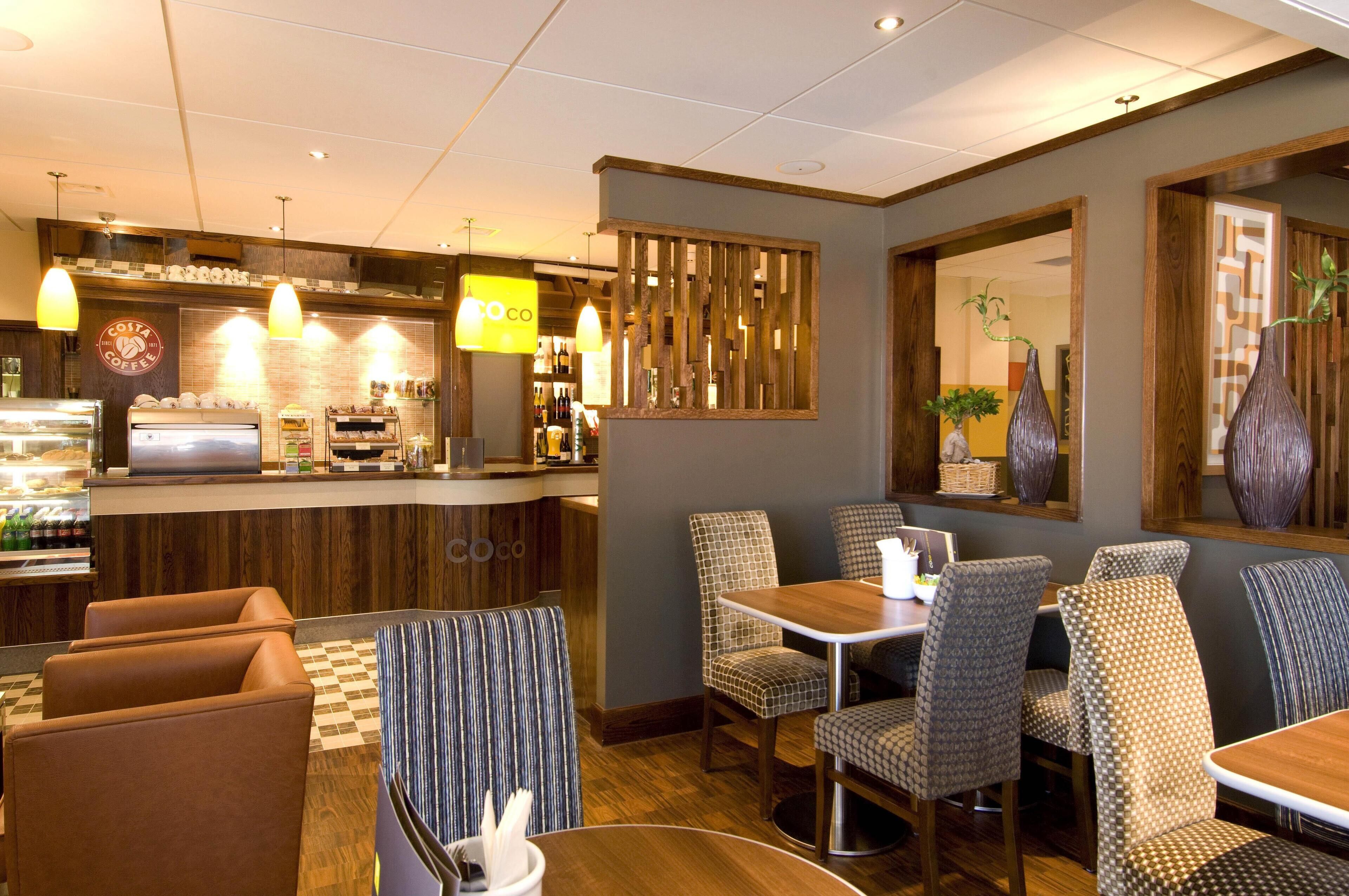 A restaurant with a counter, chairs, tables, and hanging lights.