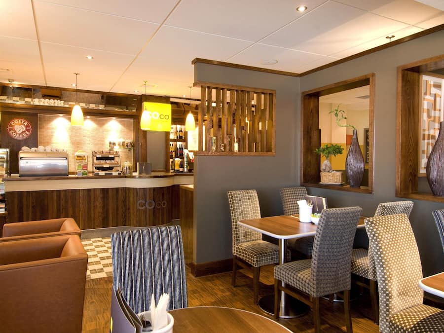 A restaurant with a counter, chairs, tables, and hanging lights.