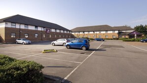 A parking lot with several cars, a building with a flat roof, and a sign indicating a Premier Inn. - Premier Inn Cardiff City South (Cardiff)