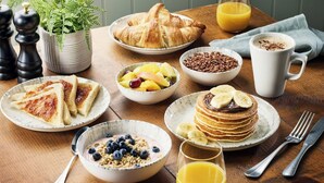 Et morgenbord med croissanter, frugt, pandekager og en kaffekop.