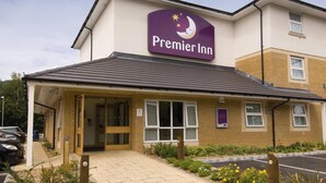 Un hotel Premier Inn con entrada despejada, zona de estacionamiento y cartel indicador.