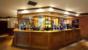 A bar area with wooden paneling, a clock, and various bottles and glasses. - Premier Inn Cwmbran (Cwmbran)