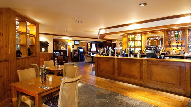 A bar area with wooden furnishings, a counter with a sign reading 'The Ashbridge,' and a seating area with tables and chairs. - Premier Inn Cwmbran (Cwmbran)