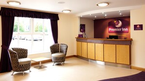 A hotel reception area with a reception desk, two patterned armchairs, and a large window with curtains. - Premier Inn Cwmbran (Cwmbran)