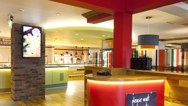 A modern interior with a reception desk, a digital screen, and a seating area. - Premier Inn Barry Island (Barry)