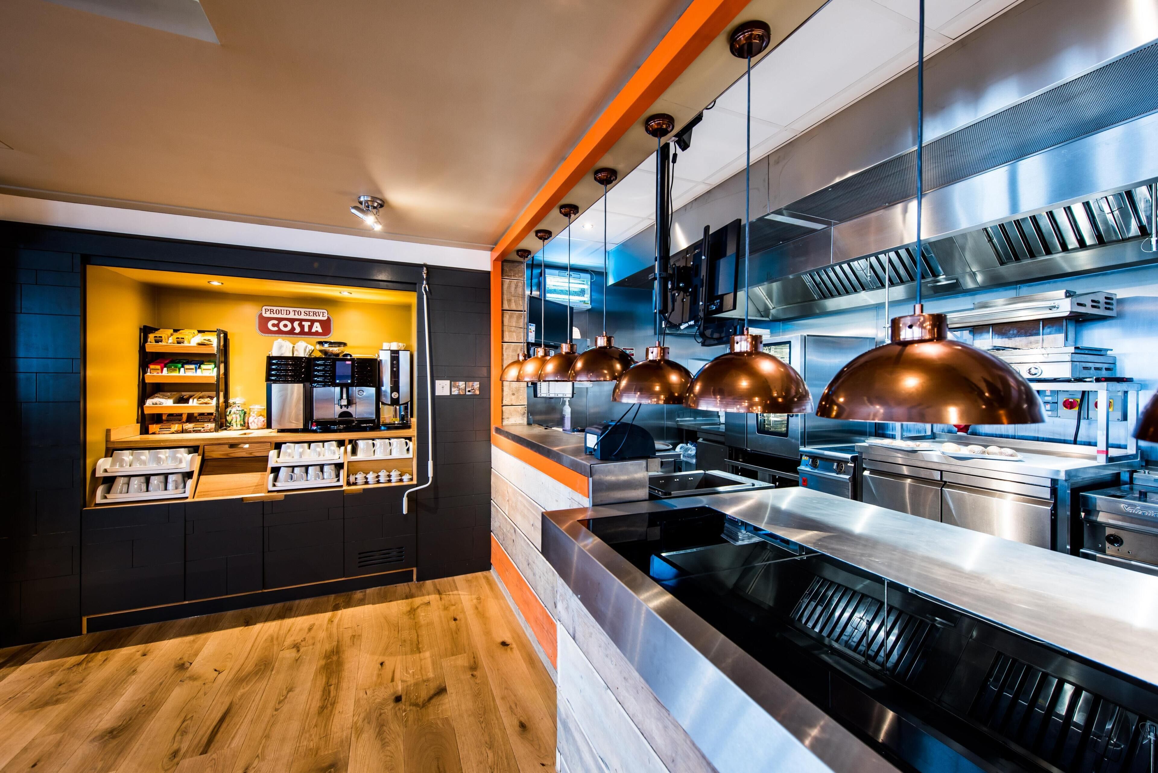 A modern kitchen with stainless steel appliances, a wooden counter, and a sign reading 'PROUD TO SERVE COSTA'.