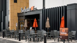 Egy szabadtéri ülőhely, ahol asztalok és székek állnak egy épület előtt, melyen egy „Beefeater” felirat látható.