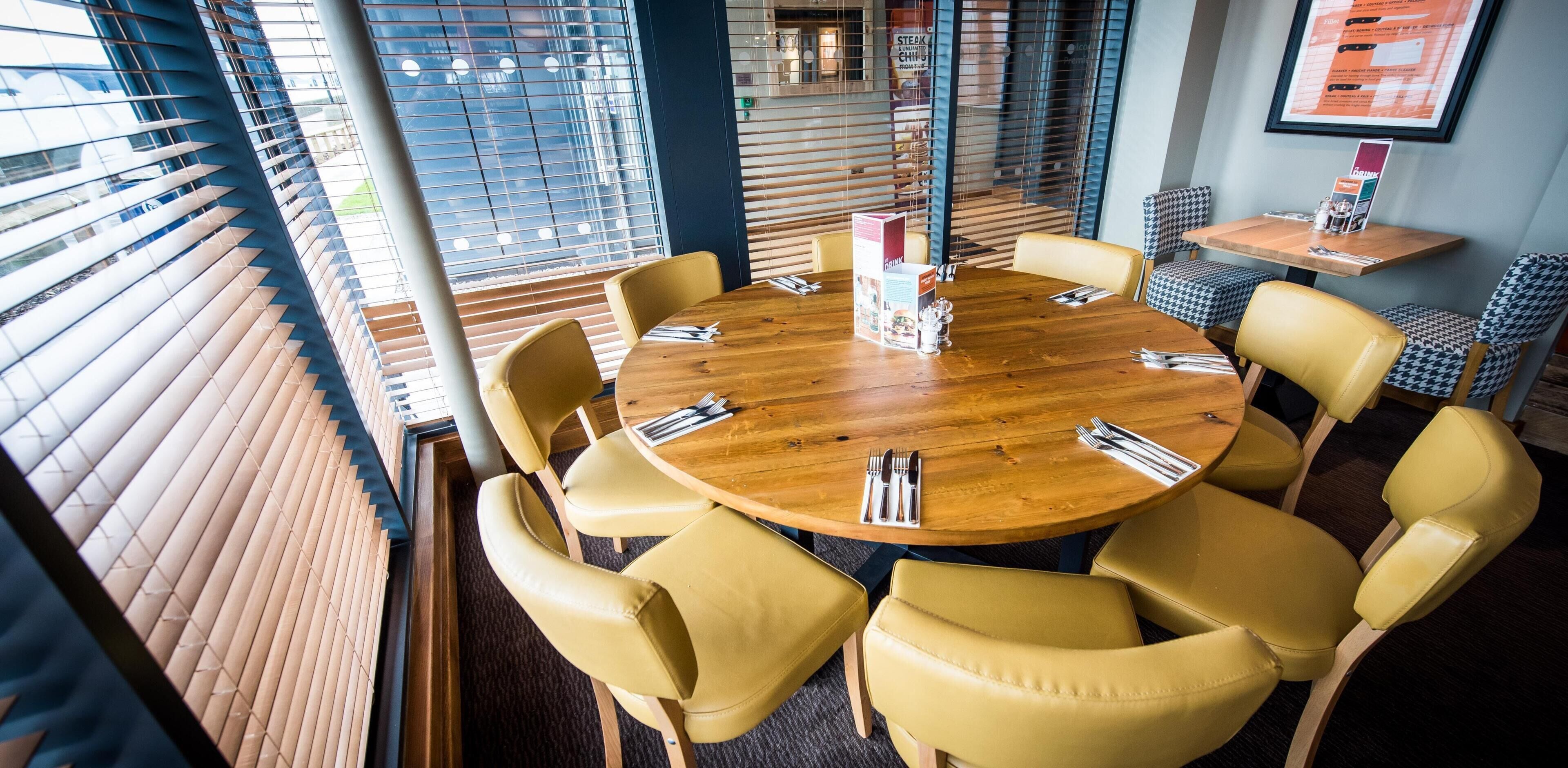 Een ronde houten tafel met gele stoelen, een menukaartstandaard en een menukaartstandaard met een menukaart.