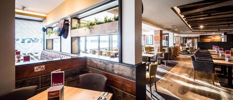 Un restaurante con un interior moderno, mesas de madera y vistas amplias a través de grandes ventanales.