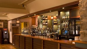 Een bar met een geldautomaat, verschillende tappunten en een ruim aanbod aan flessen en glazen.