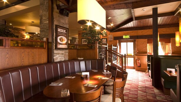 Een restaurant met een houten inrichting, een hoge plafond en een grote eettafel met stoelen.