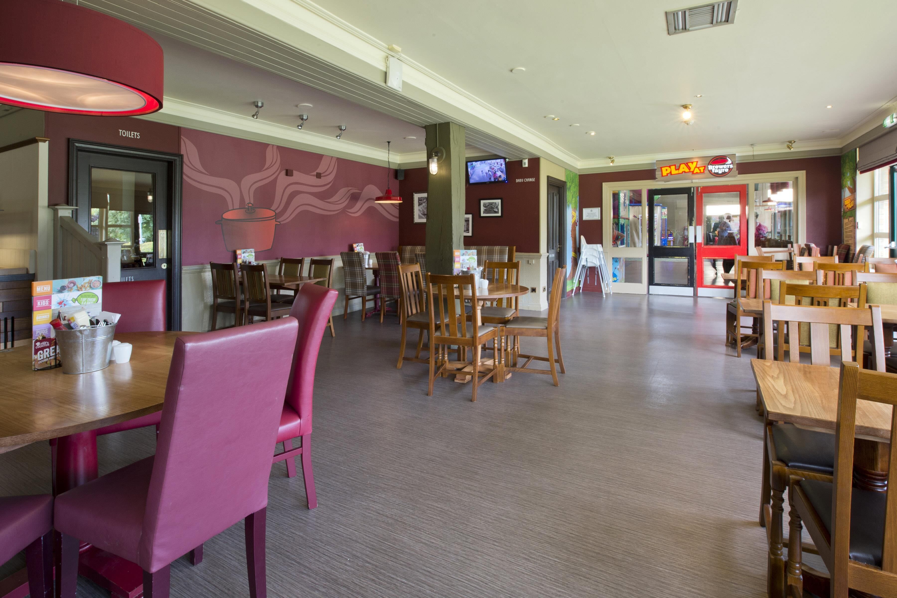 Interior de un restaurante con varias mesas y sillas, un televisor en la pared y un letrero que indica una zona de juegos.