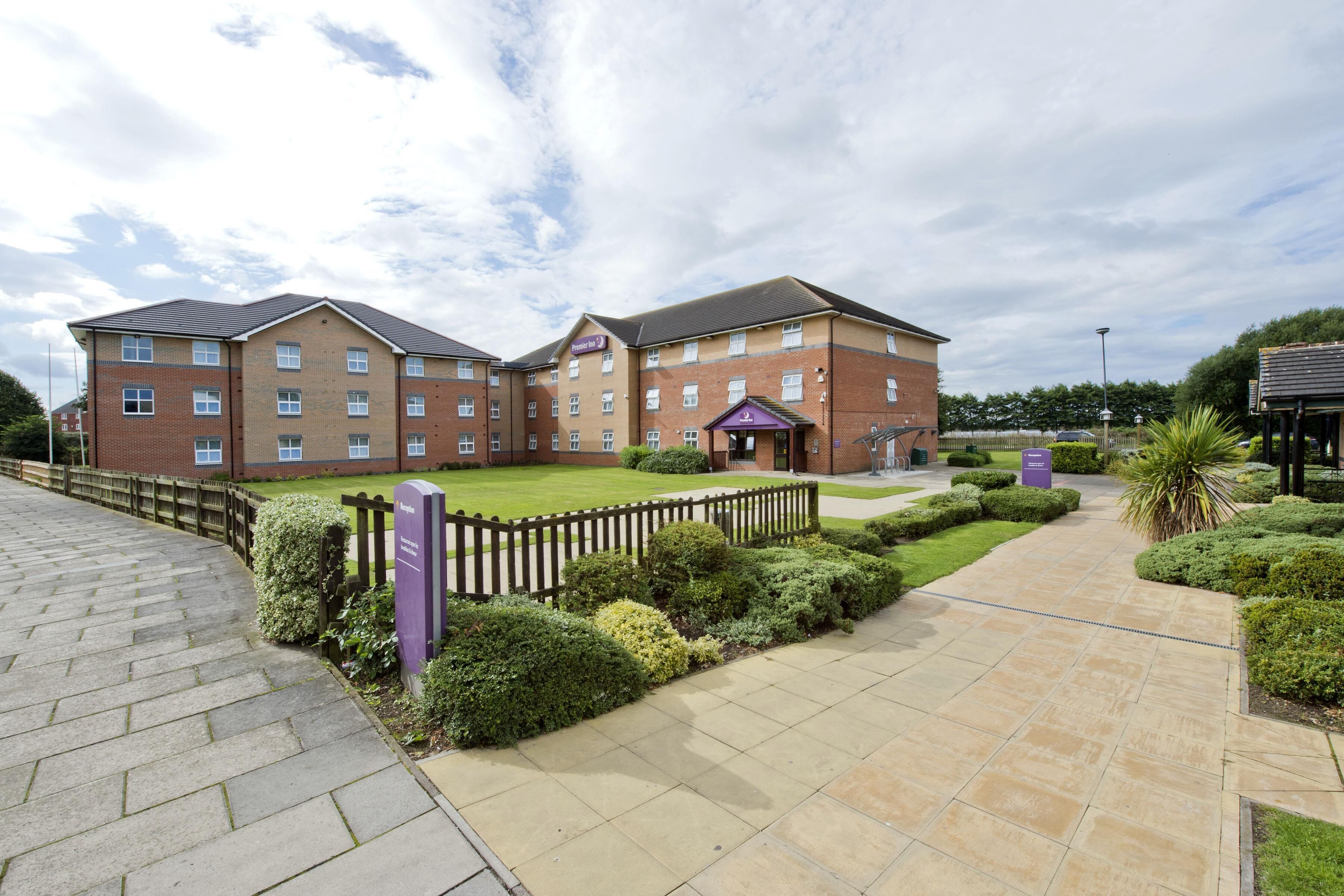 A multi-story hotel with a brick facade, a central entrance with a purple canopy, and a well-maintained garden area.