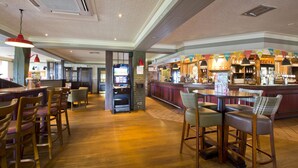 A bar area with wooden flooring, bar stools, a jukebox, and a counter with a variety of bottles. - Premier Inn Doncaster Central East (Doncaster)