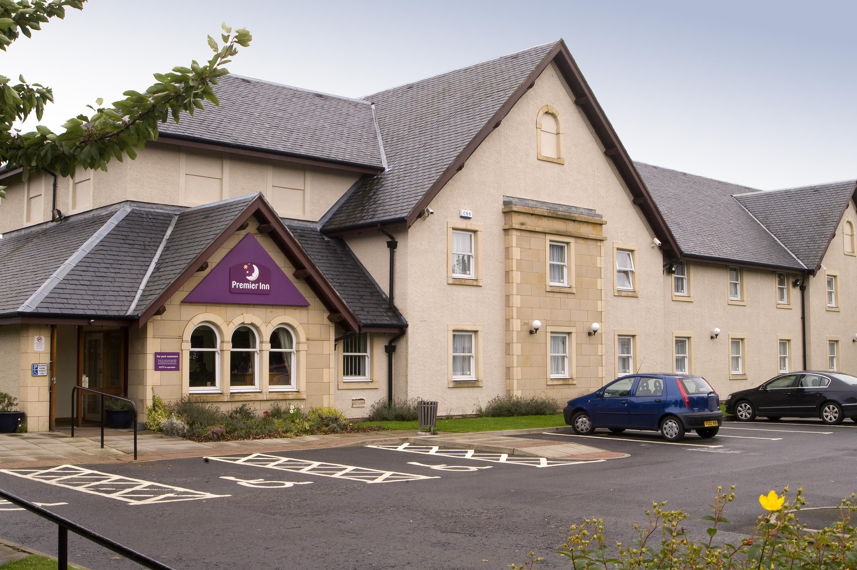 En bygning med et skilt, der viser 'Premier Inn', og et parkeringsområde med afmærkede parkeringspladser.