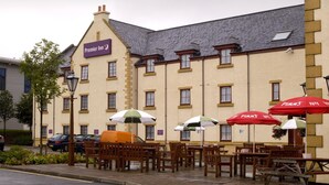 A hotel with outdoor seating, a sign for 'Premier Inn,' and a parked van. - Premier Inn Edinburgh A1 - Newcraighall (Musselburgh)