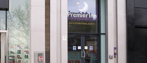 Een hotelingang met een glazen gevel, een bord met de tekst Premier Inn, en schoenen die voor de deur staan.