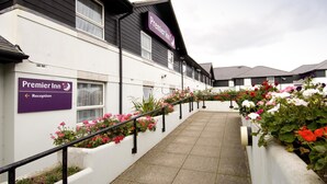 Un hôtel appelé « Premier Inn », avec un panneau indiquant la réception, un chemin et des parterres de fleurs le long du trottoir.