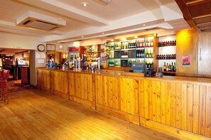 Un coin bar avec des lambris en bois, une horloge et diverses bouteilles exposées sur des étagères.