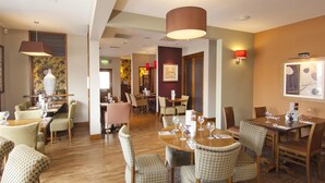 A hotel dining area with multiple tables and chairs, a large vase, and a wall-mounted light fixture. - Premier Inn Exeter Central St Davids (Exeter)