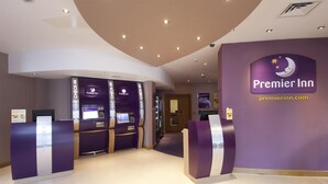 A Premier Inn reception area with a purple theme, check-in counters, and a visible website address. - Premier Inn Exeter Central St Davids (Exeter)