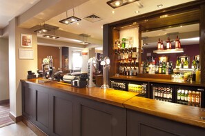 A bar area with a counter, bar stools, and a variety of bottles and glasses.