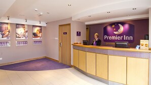 A hotel reception area with a counter, a receptionist, and a wall with the hotel's logo. - Premier Inn Paignton South - Brixham Road (Paignton)