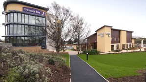 A Premier Inn hotel with a glass facade, a separate building labeled 'Beefsteak Grill,' and a well-maintained lawn area. - Premier Inn Paignton South - Brixham Road (Paignton)