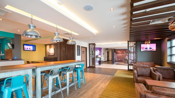 A modern hotel lobby with a bar area, seating, and a television screen. - Premier Inn Exmouth Seafront (Exmouth)