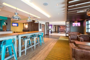 Un hall d’hôtel moderne doté d’un bar, de coins salon et d’un écran de télévision.