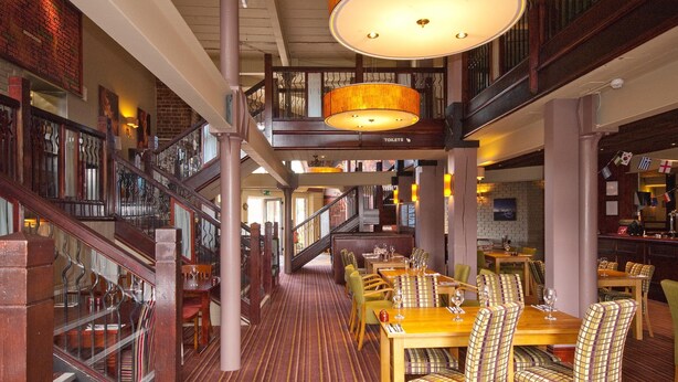 A multi-level restaurant with wooden flooring, striped chairs, and a staircase.