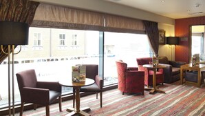 A hotel room with a large window, a sofa, a chair, a small table, and a lamp. - Premier Inn Camberley (Camberley)