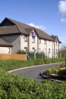 A multi-story hotel with a brown roof, a wooden fence, and a well-maintained garden area.