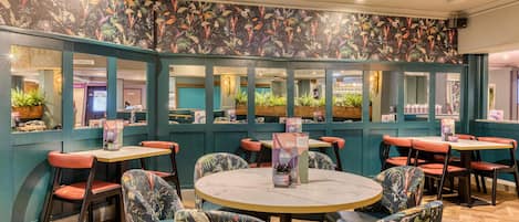 Un restaurante con mesas redondas, sillas con estampado floral y una pared con temática tropical.