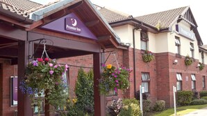 En hotellentrén med en skylt som visar texten ”Premier Inn”, ett överbyggt entréområde och hängande blomkorgar.