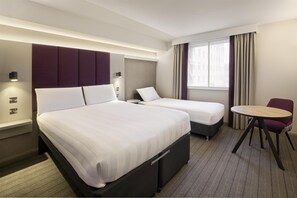 Ein Hotelzimmer mit zwei Betten, einem kleinen Tisch, einem Stuhl und einem Fenster mit Vorhängen.