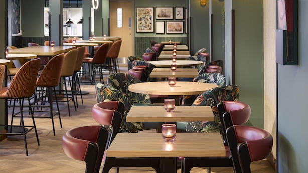 L’intérieur d’un restaurant avec des tables rondes, des chaises rembourrées et des lampes suspendues fixées au mur.
