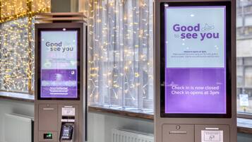 Two self-service kiosks with screens displaying check-in information and a message welcoming guests.