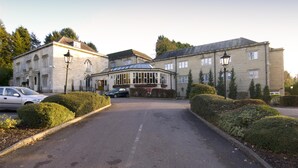 A building with a central entrance, a parking area, and well-maintained hedges.
