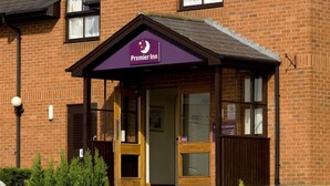 Un bâtiment en briques avec une enseigne « Premier Inn », une entrée en bois et un petit jardin.