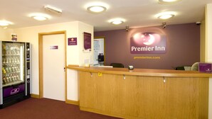 Un'area reception di un hotel con una scrivania in legno, una macchina distributrice e un cartello con la scritta Premier Inn.