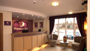 Een hotel receptie met een receptiebalie, twee fauteuils, een bijzettafeltje en een raam met gordijnen.