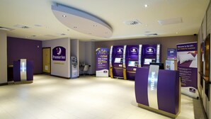 A hotel reception area with a modern design, featuring a reception desk, self-service kiosks, and informational posters. - Premier Inn Glasgow Cc Buchanan Galleries (Glasgow)
